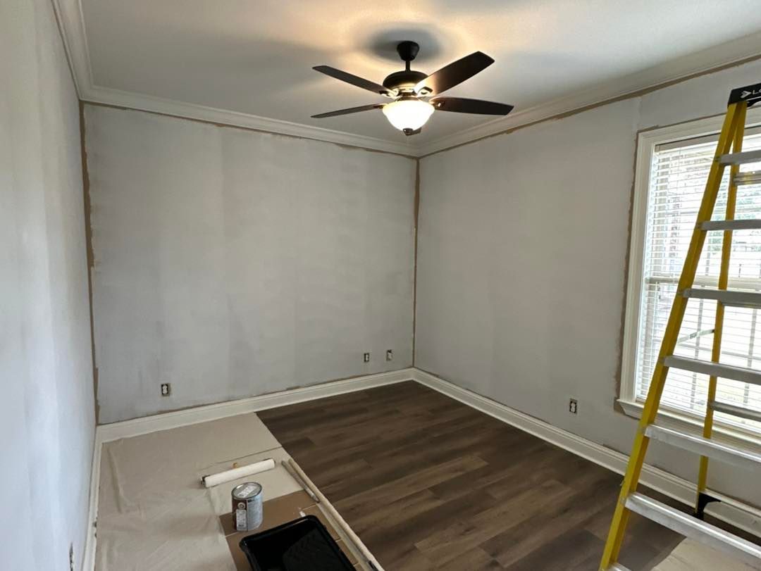 Empty room with gray walls, wood floor, ceiling fan, and a yellow ladder by the window.