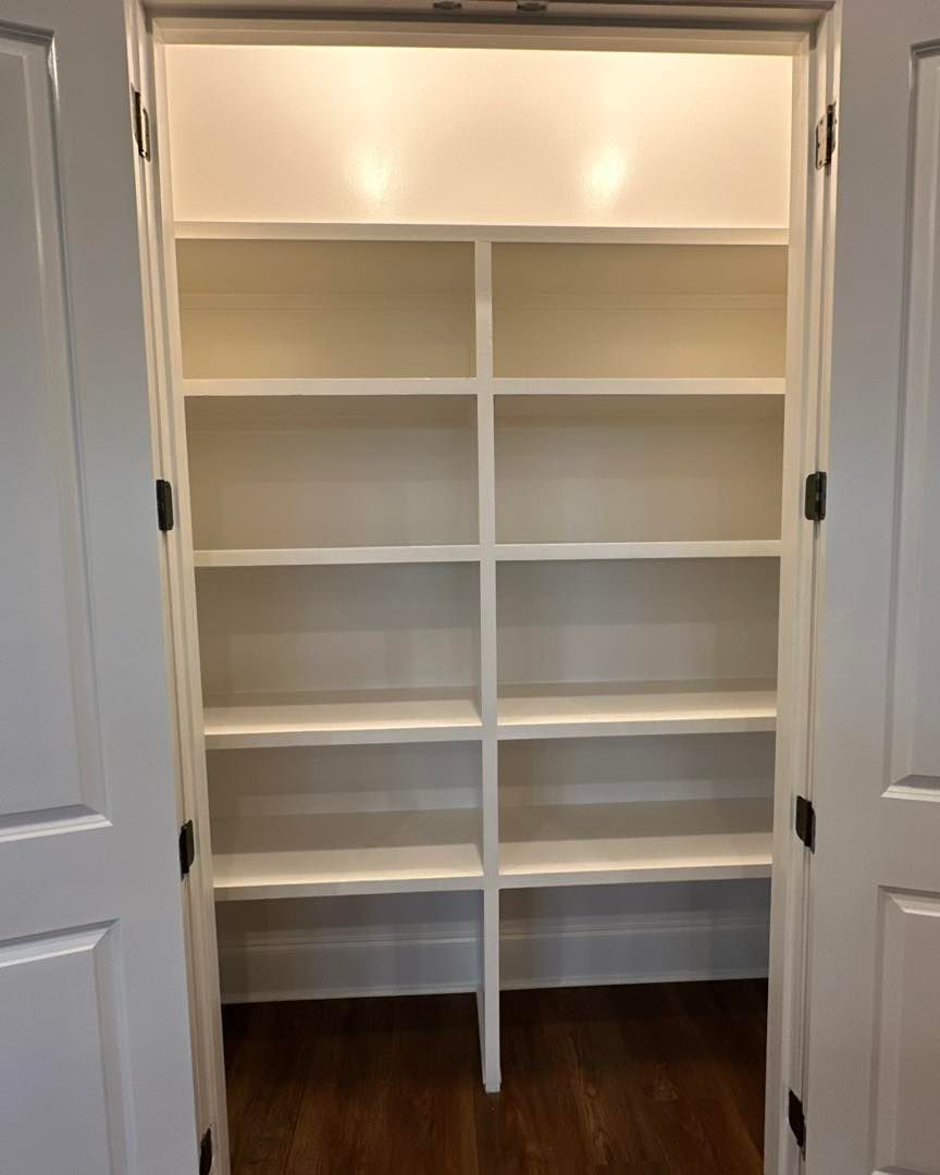 White built-in closet shelves with drawers, framed by open double doors and hardwood floor.