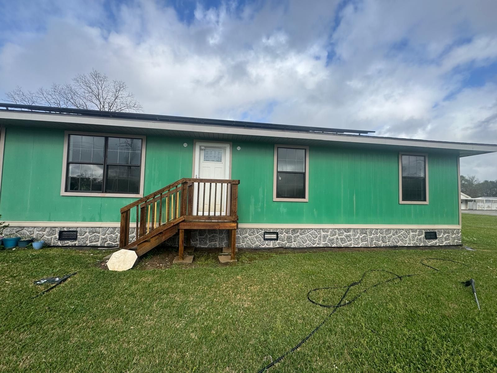 Green house with a small front porch, white trim, and a grassy yard under a cloudy sky.