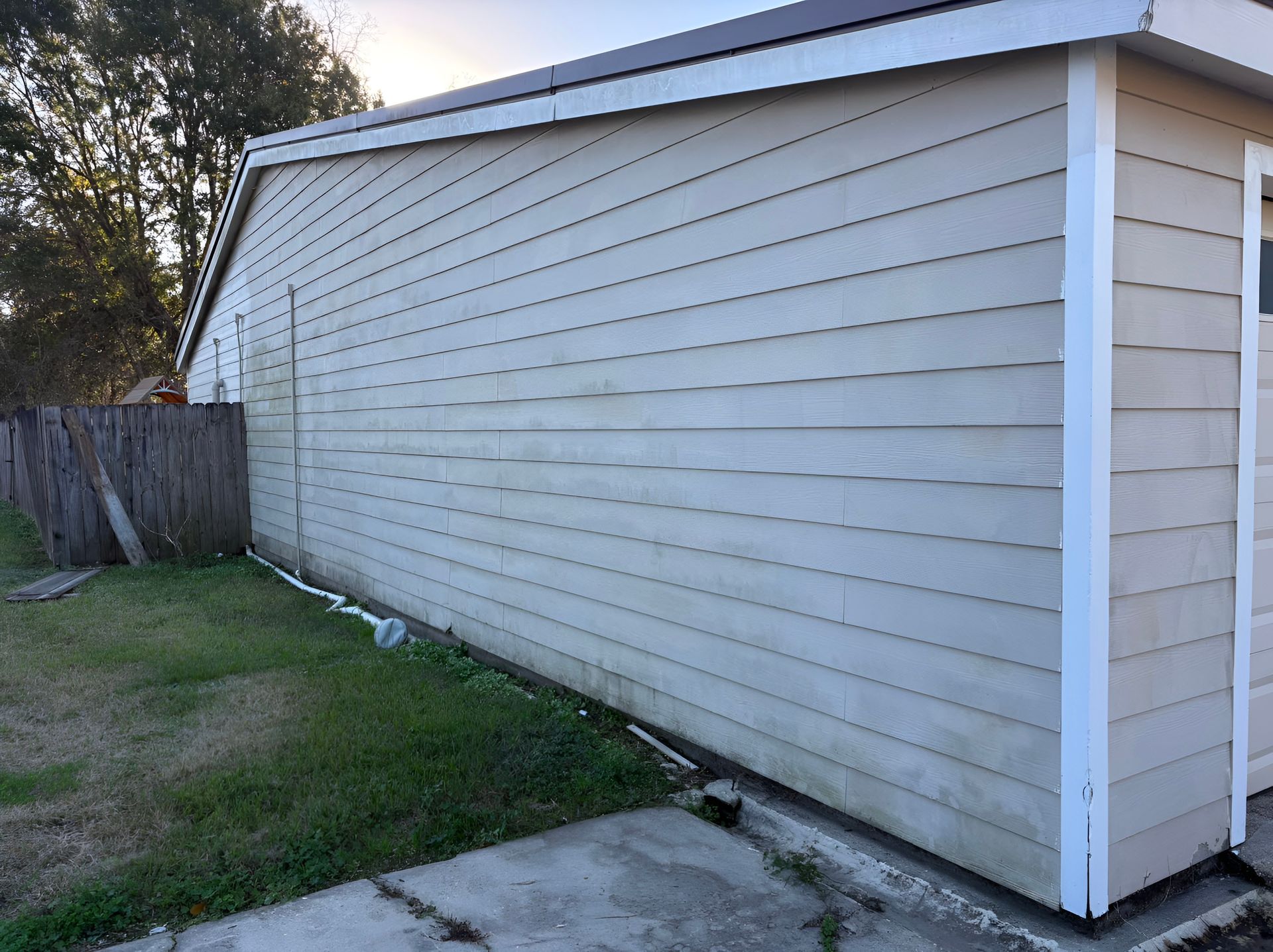Side view of a light gray house exterior with white trim, a fence, and a concrete walkway.