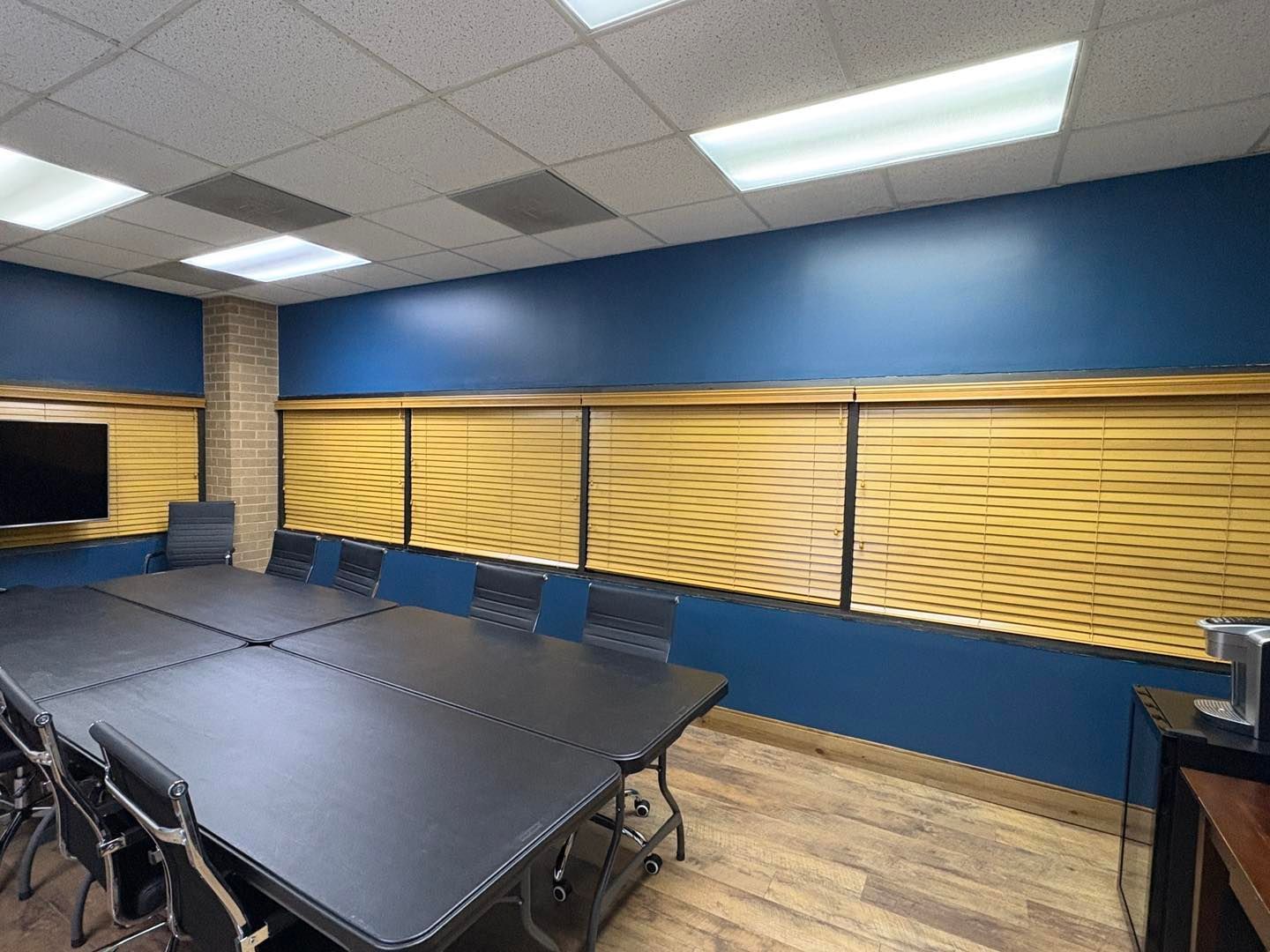 Empty conference room with black tables, chairs, blue walls, and fluorescent ceiling lights.