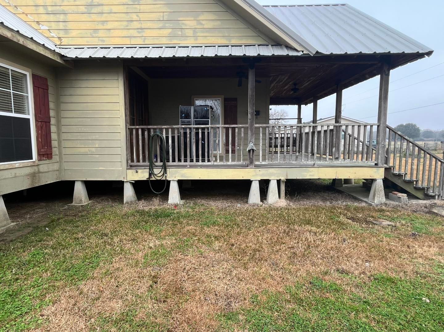 Weathered house porch with white railings, metal roof, and steps over patchy grass