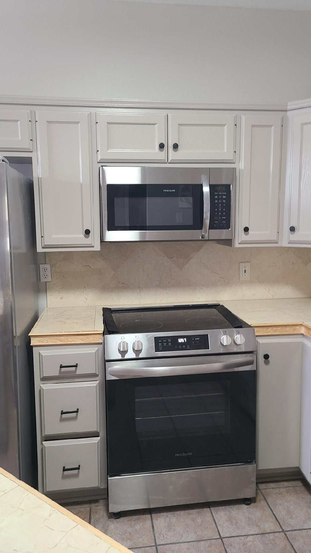 White kitchen with stainless steel stove and microwave, white cabinets, and beige countertops.