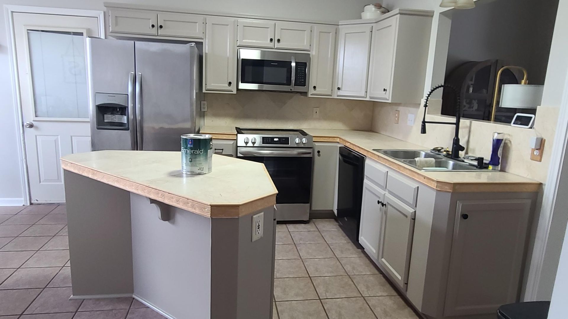Bright kitchen with white cabinets, stainless steel appliances, and a central island on tiled floor