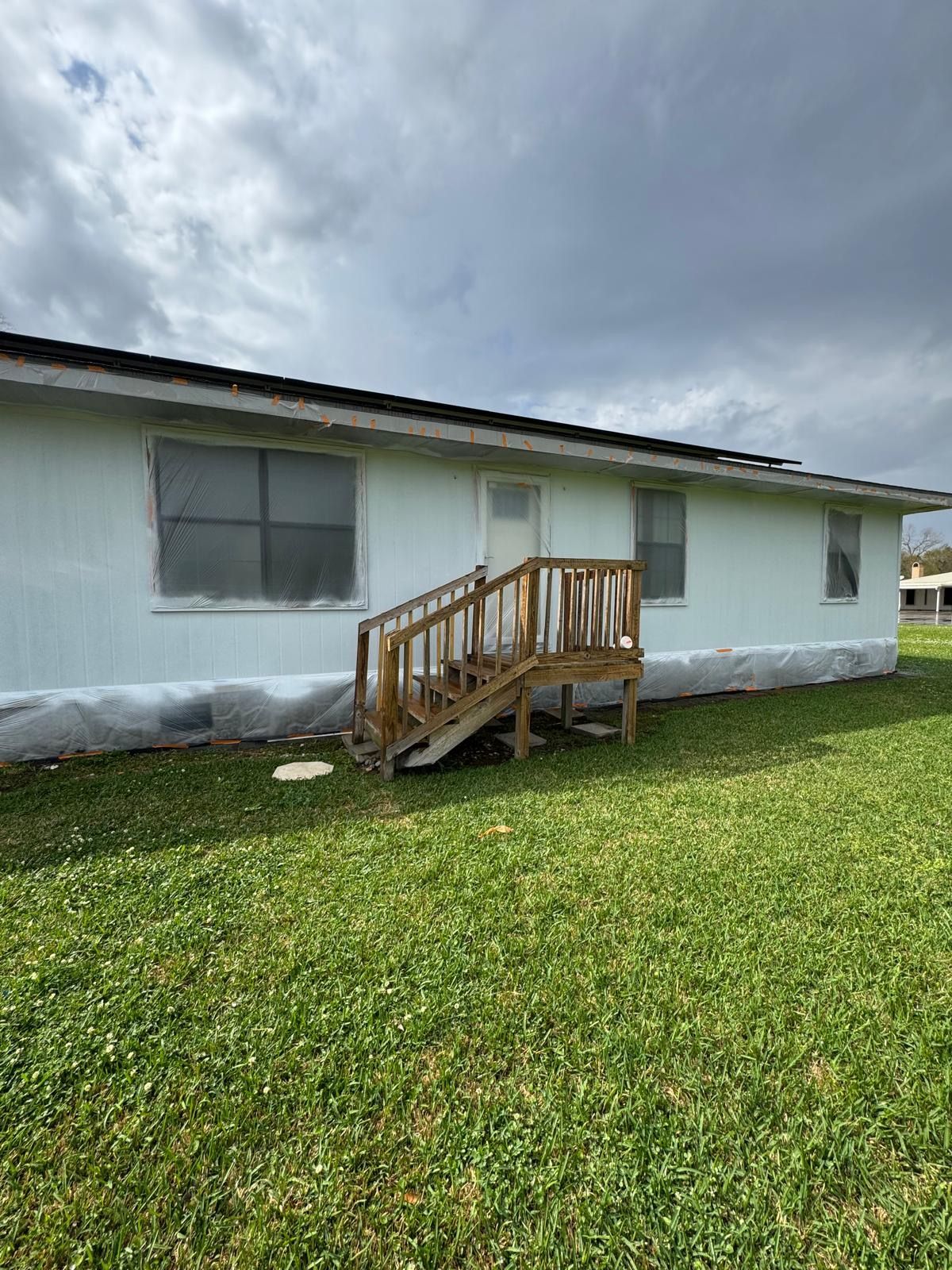 White house exterior with a small wooden ramp on a grassy yard under a cloudy sky