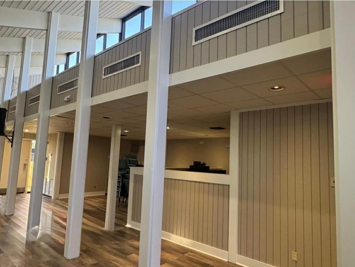 Empty indoor hallway with white columns, wood paneling, and high windows in soft daylight