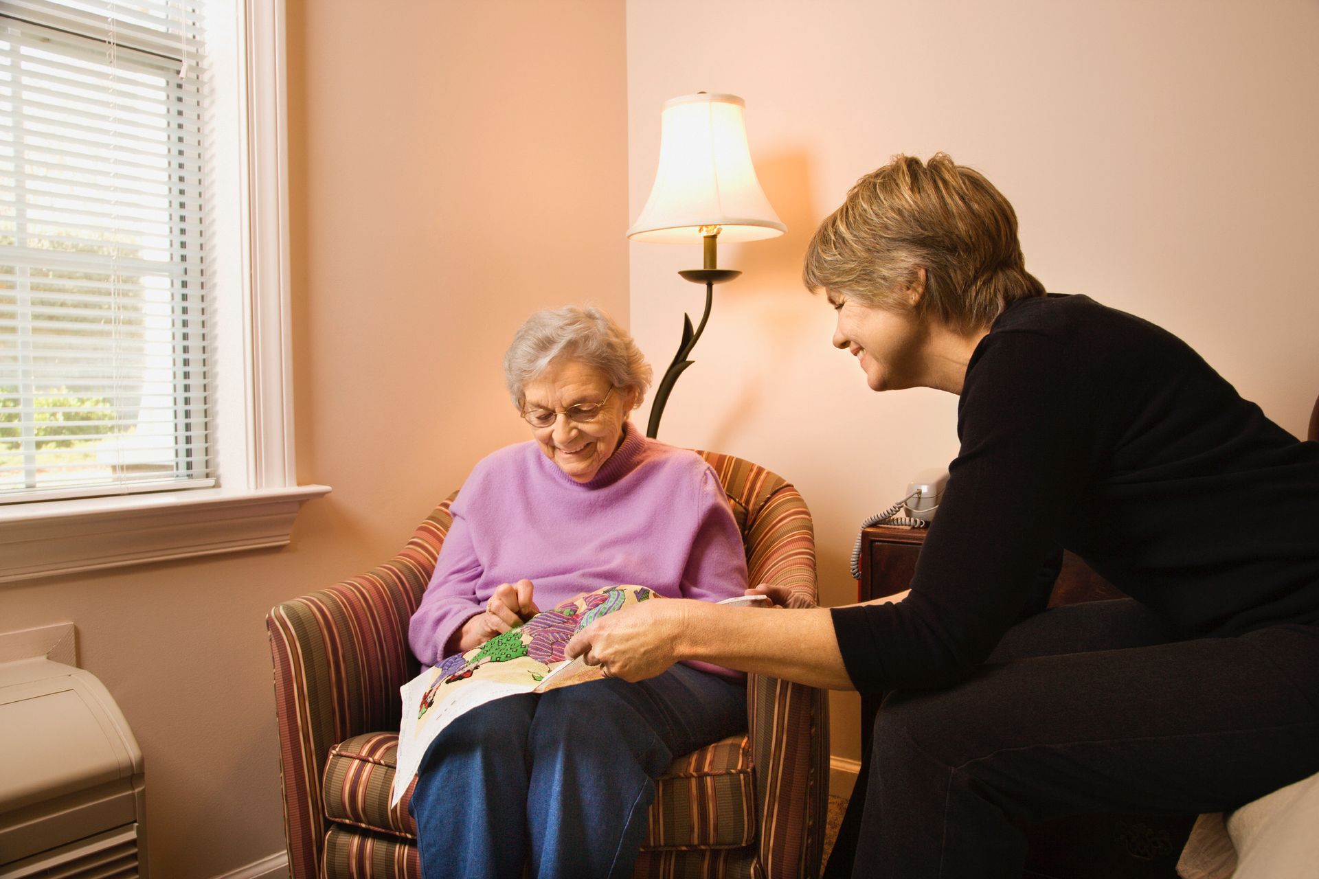 Woman assists elderly person with crafting in a well-lit room.
