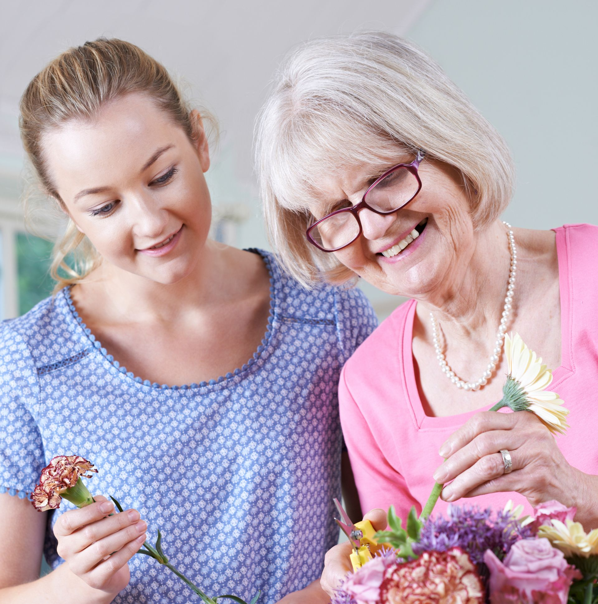 Woman helping elderly person arrange flowers; both smiling.