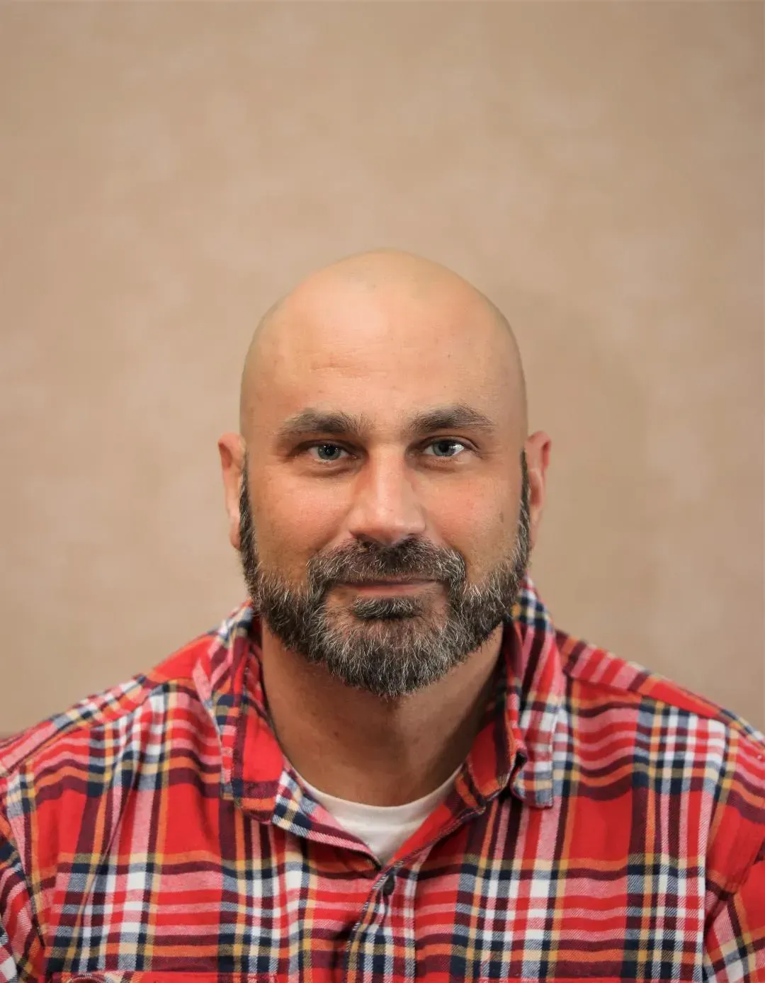 Bald man with a full beard wearing a red and white plaid shirt.