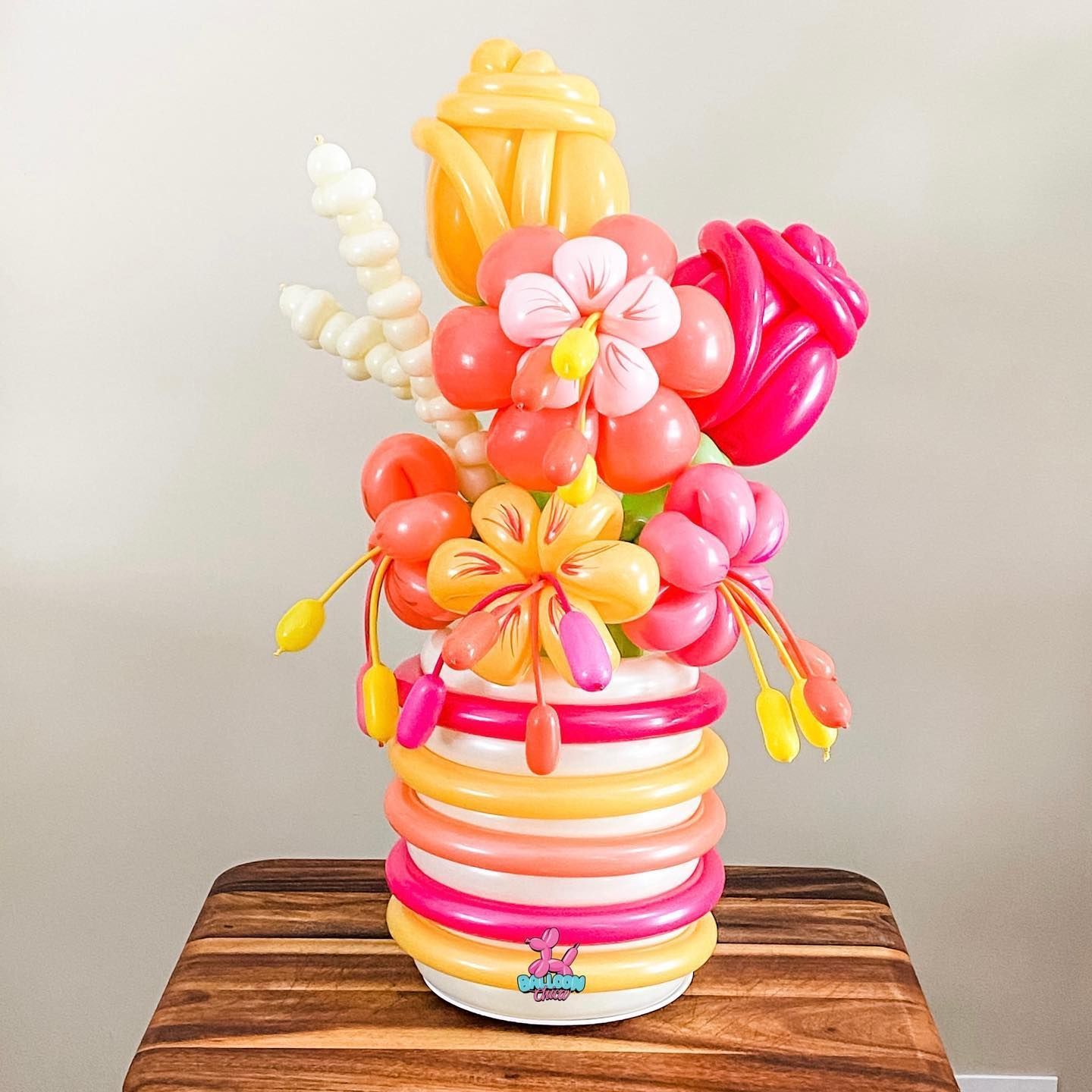 a vase filled with balloons and flowers is sitting on a wooden table