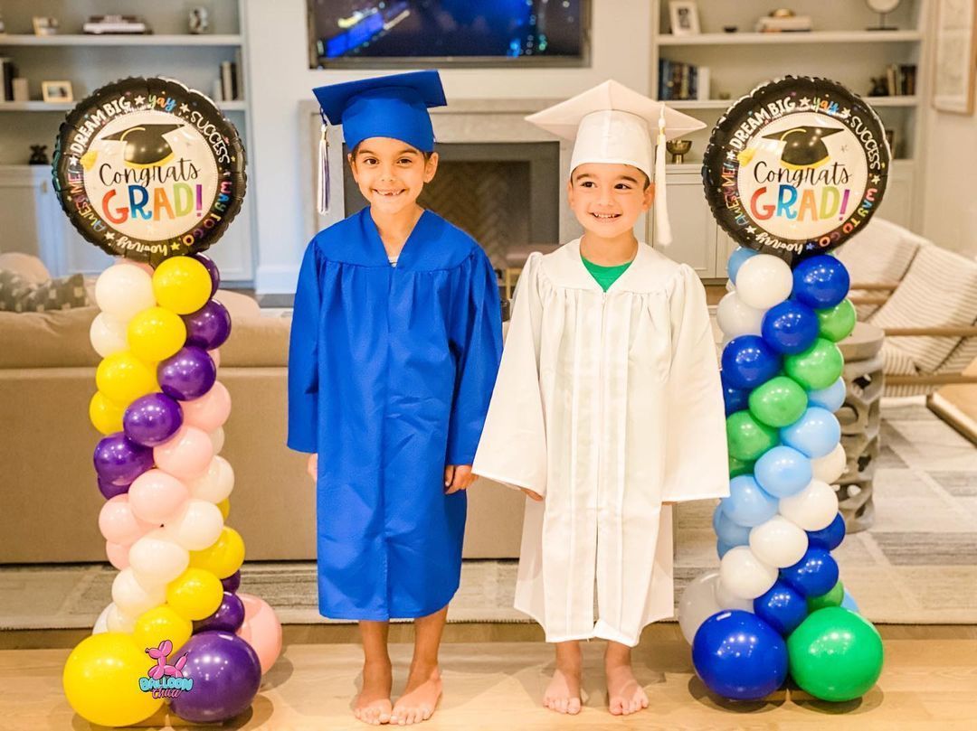 two boys in graduation caps and gowns are standing next to balloons