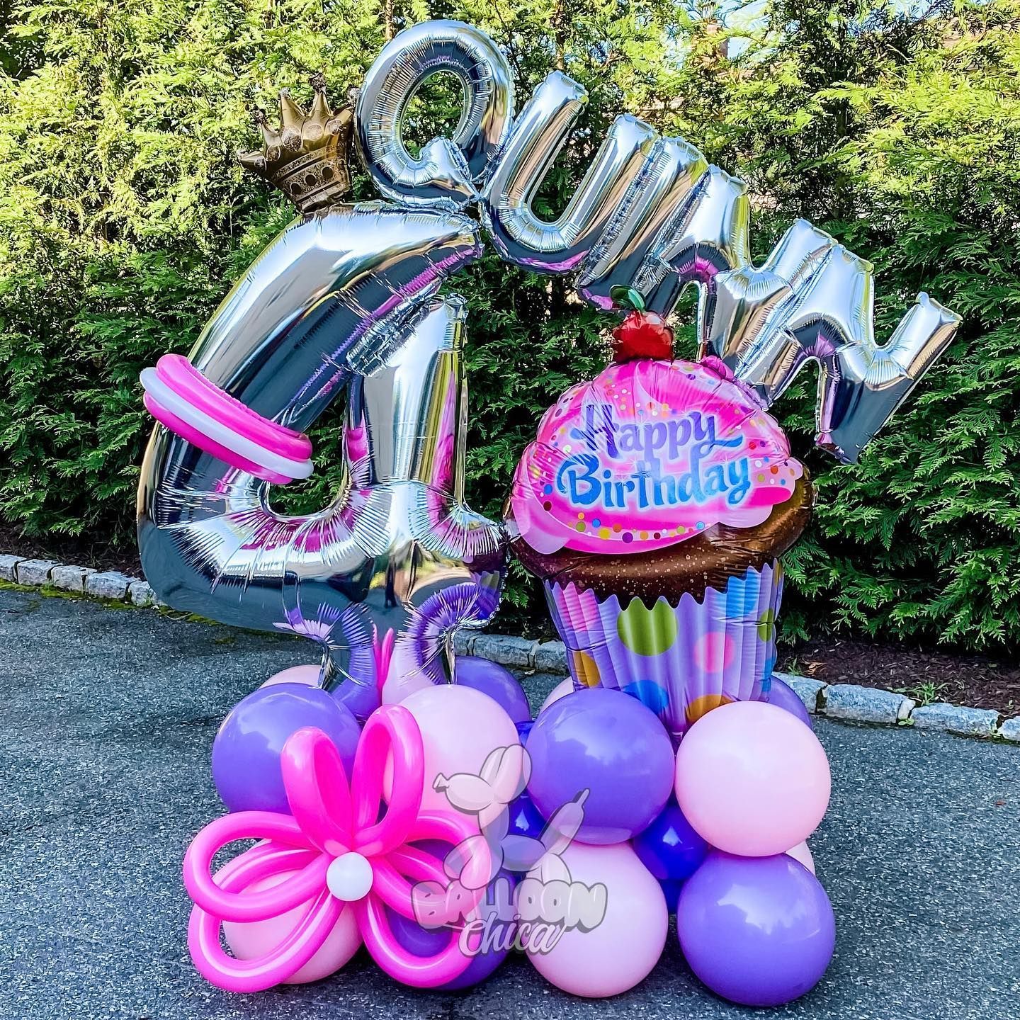 a bunch of pink and purple balloons with a cupcake on top of them