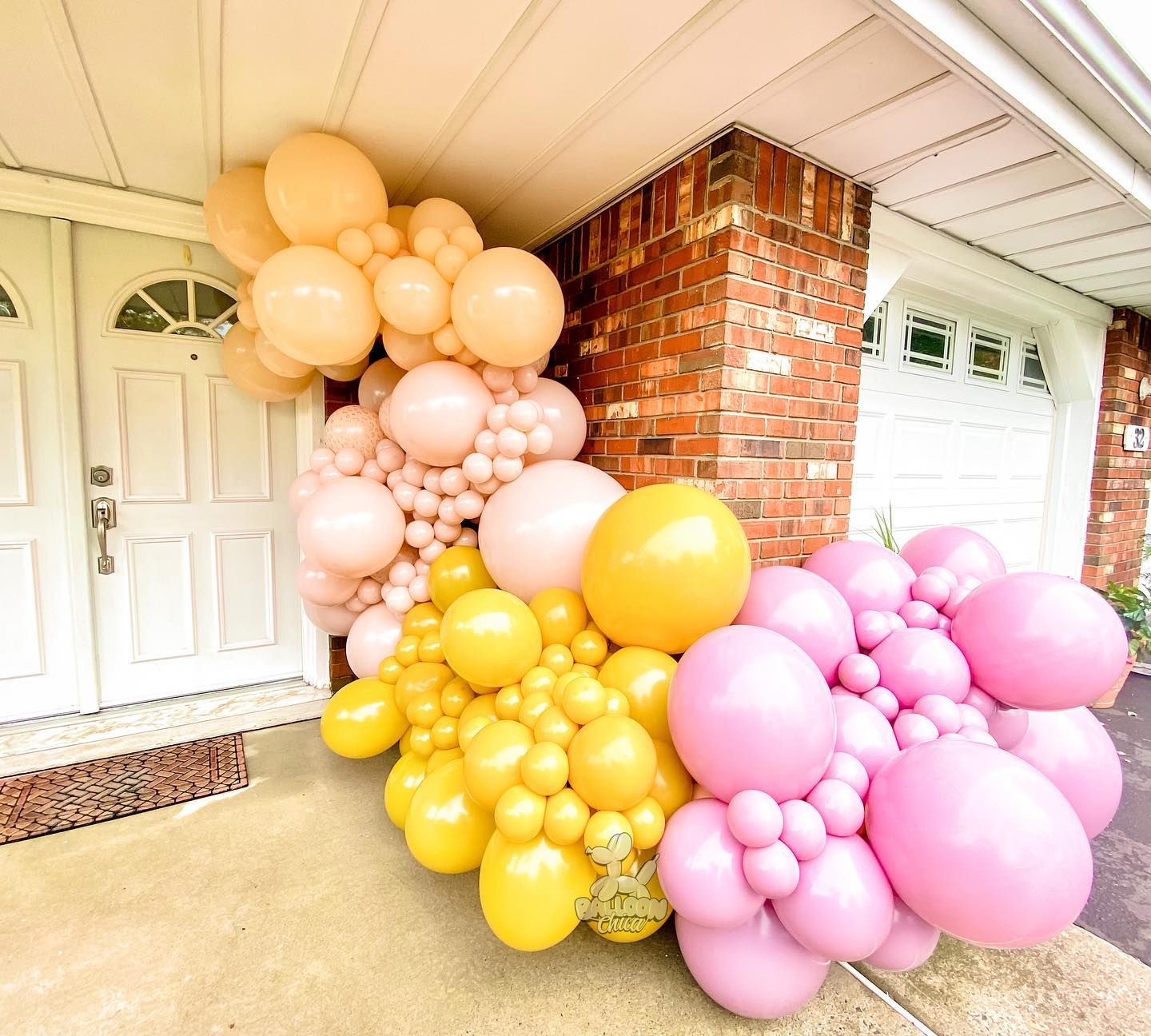 a bunch of pink and yellow balloons are sitting in front of a brick building