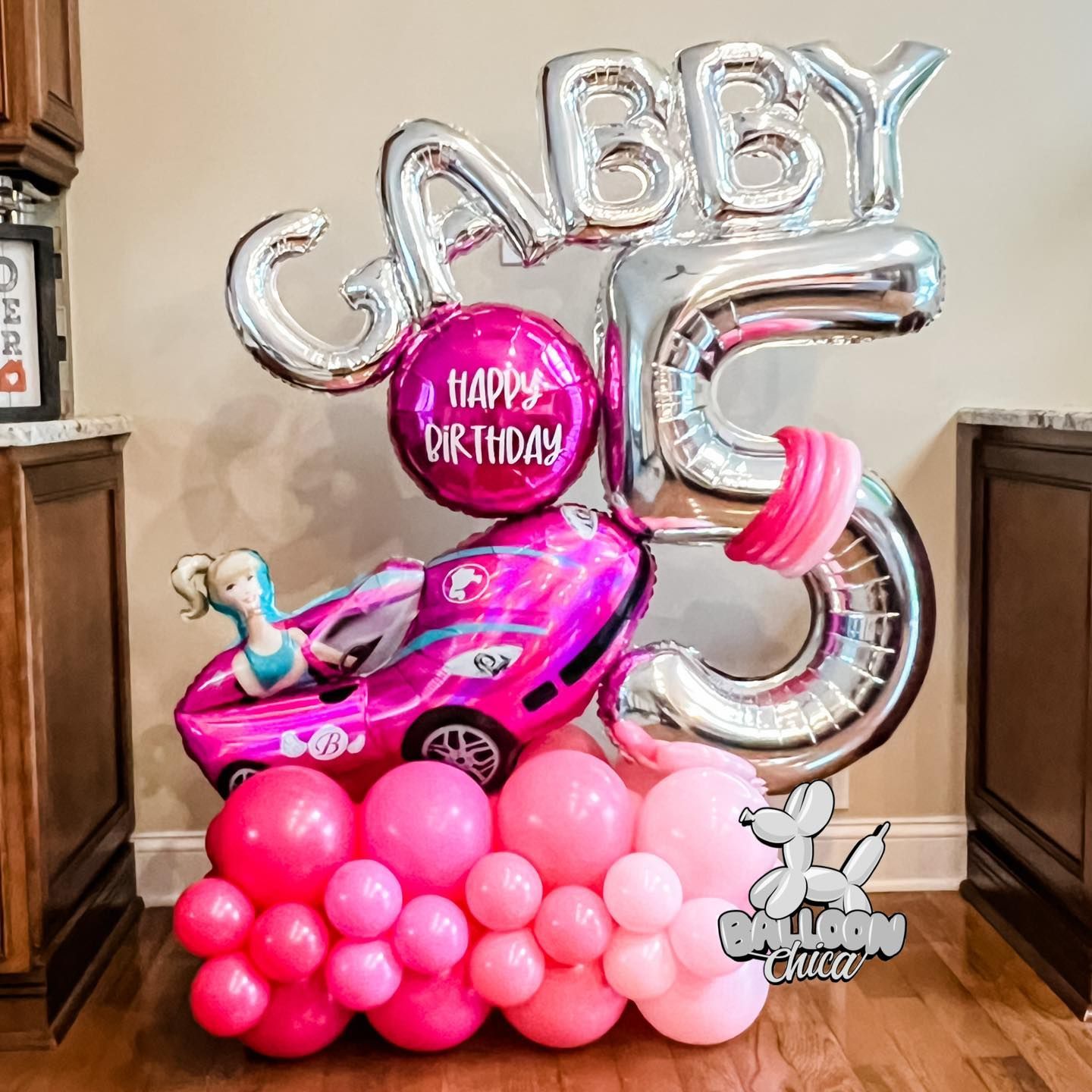 a girl is celebrating her 5th birthday with balloons and a barbie car