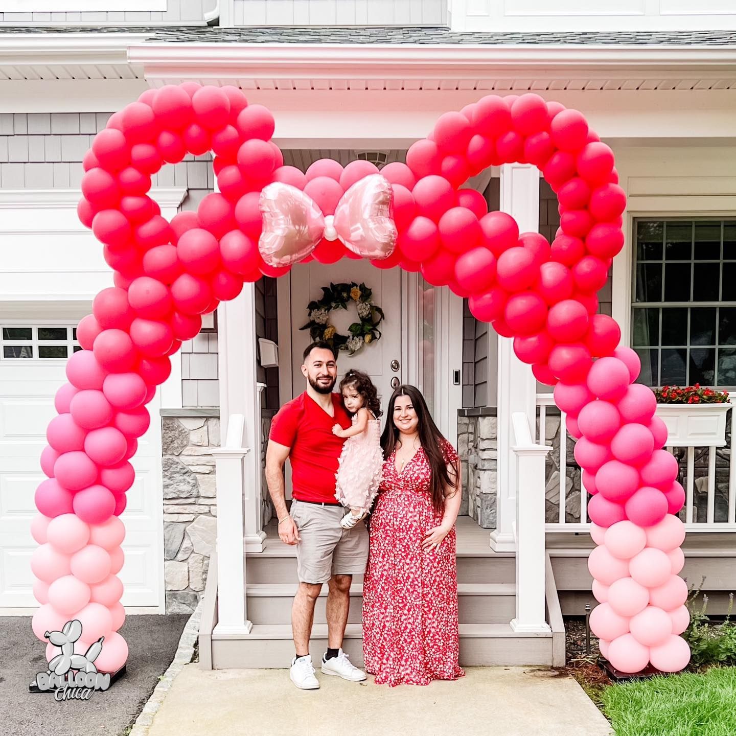 a family is standing in front of a house decorated with pink balloons