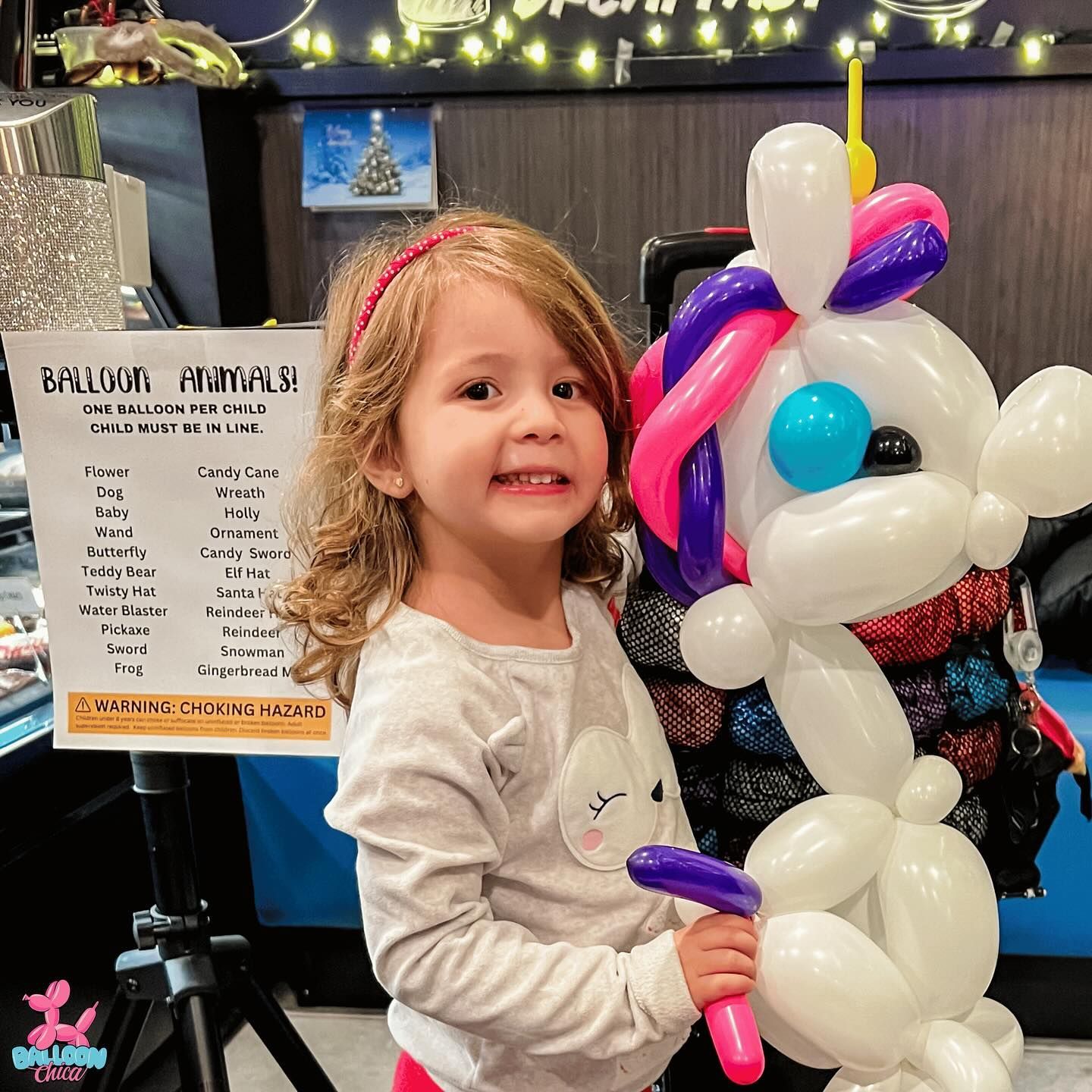 a little girl is standing next to a balloon unicorn .