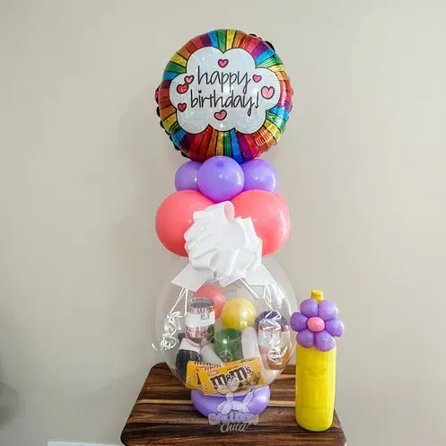 a balloon filled with candy and a happy birthday balloon is sitting on a wooden table