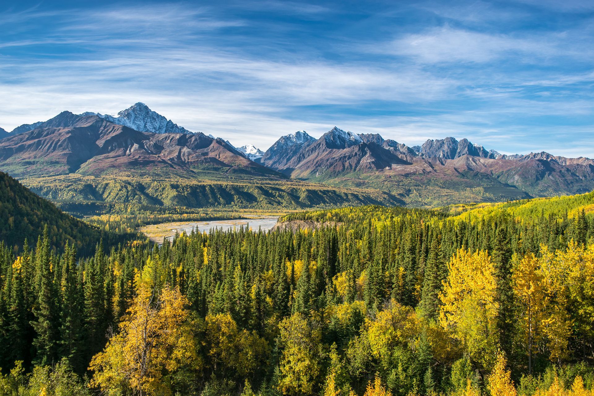 There is a lake in the middle of a forest with mountains in the background.