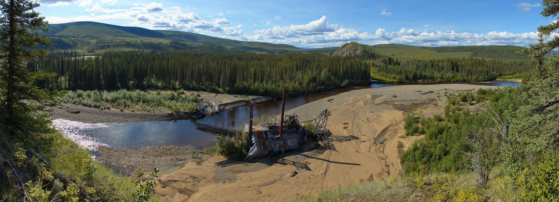 A panoramic view of a river surrounded by trees and mountains.