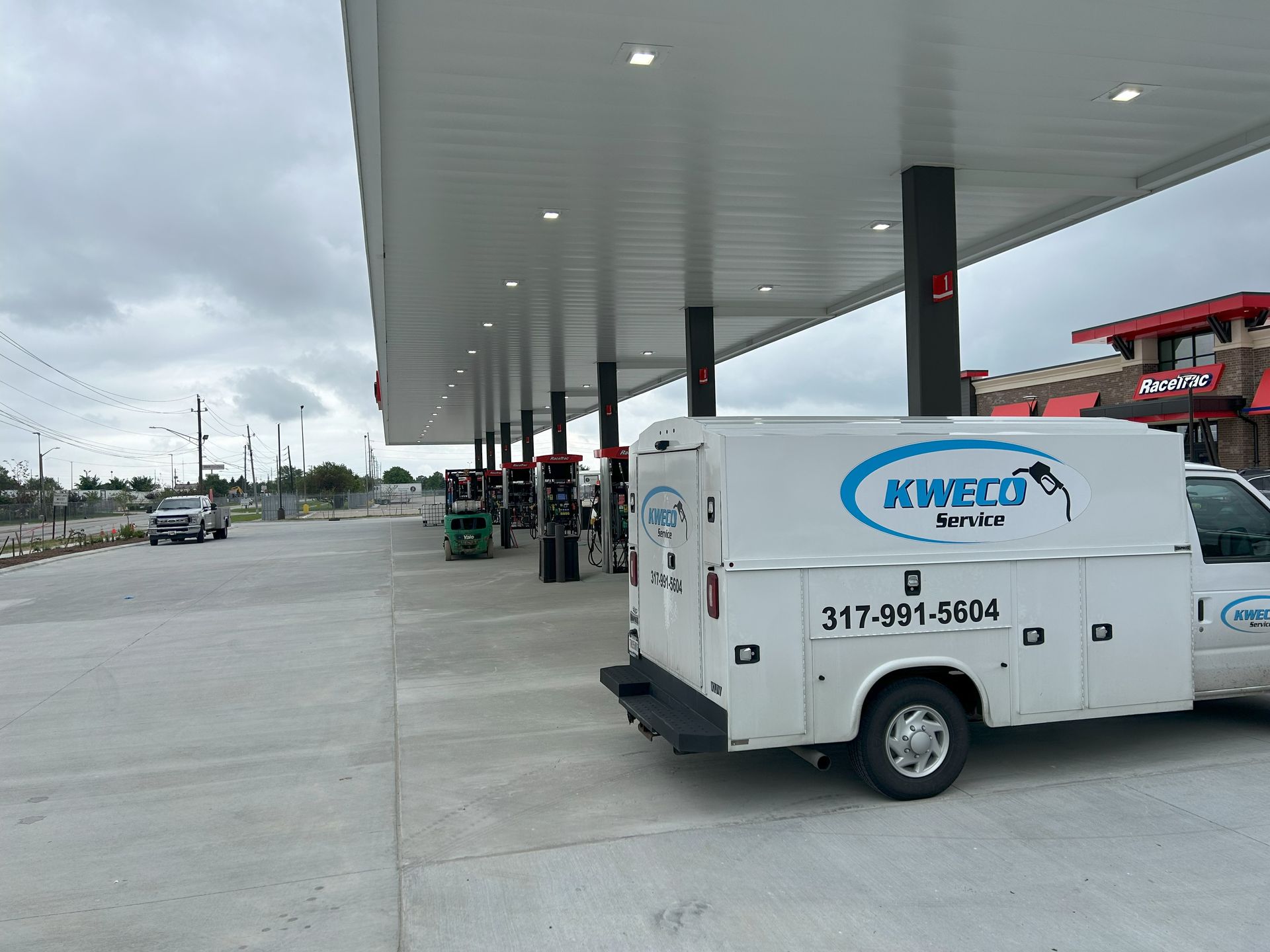 White service truck at a gas station with a canopy, cloudy sky. Truck has "KWIK Service" logo.