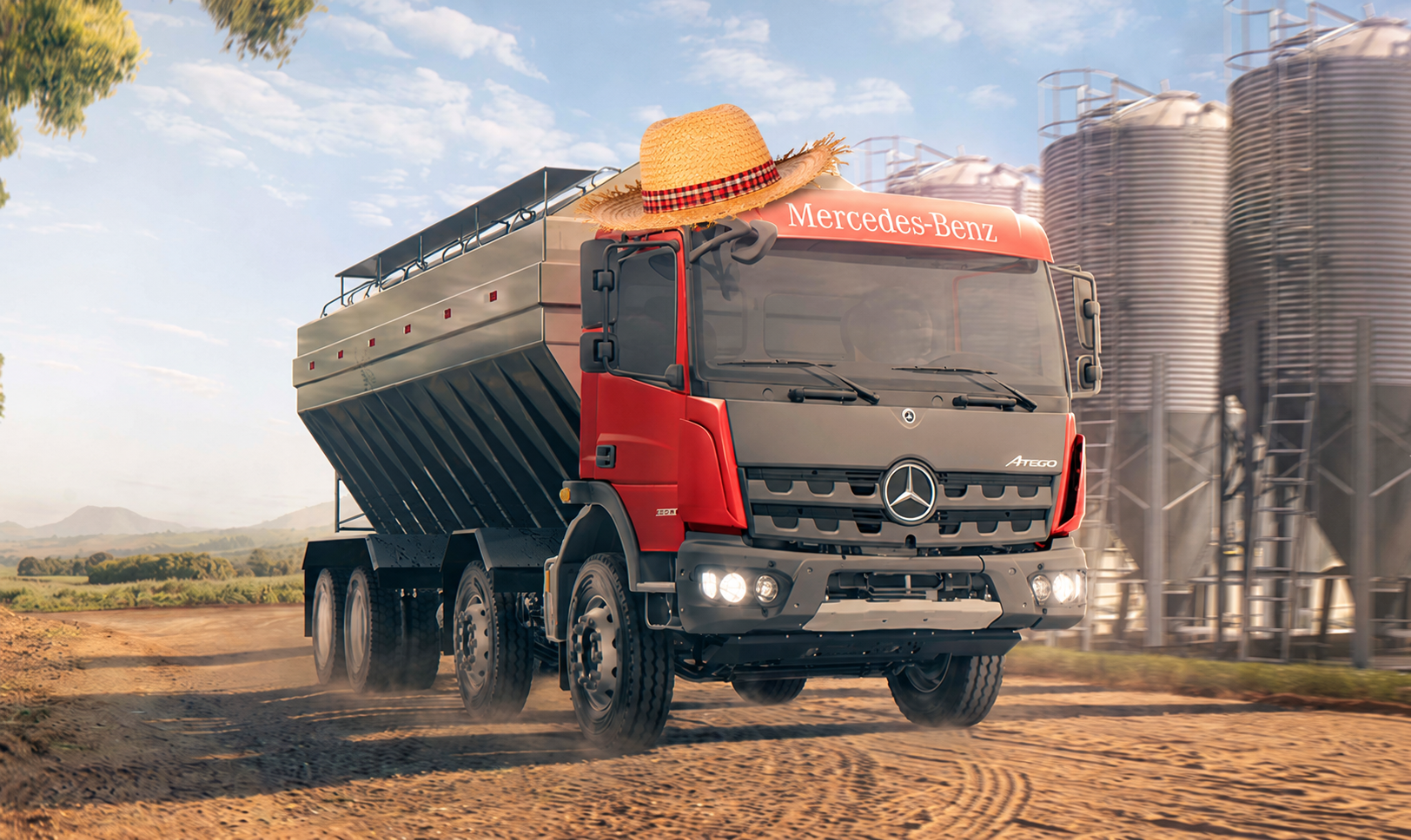 Red truck loaded with grain driving on a dusty farm road beside silos and a field