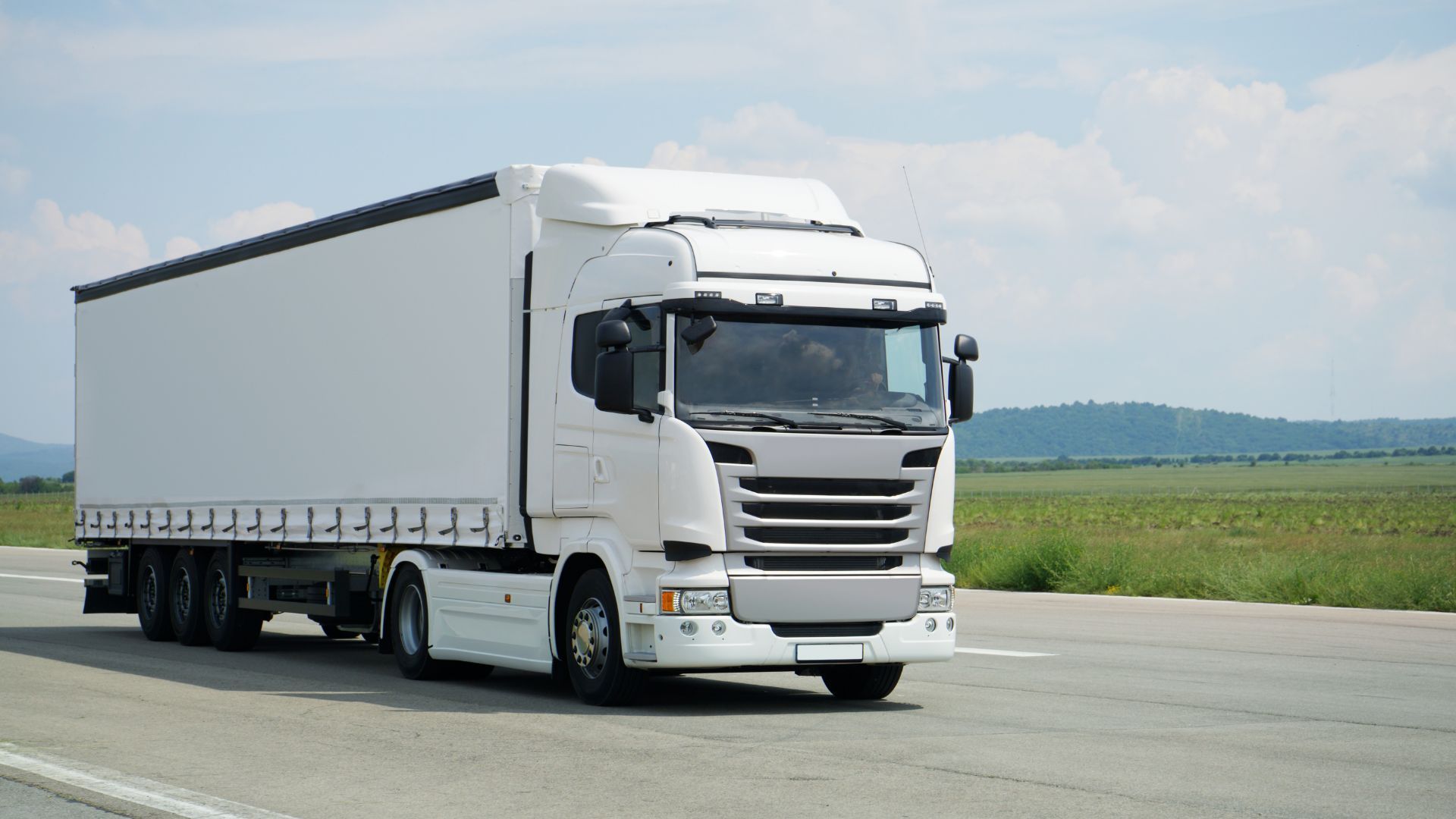 White semi-truck driving on a rural highway under a cloudy sky