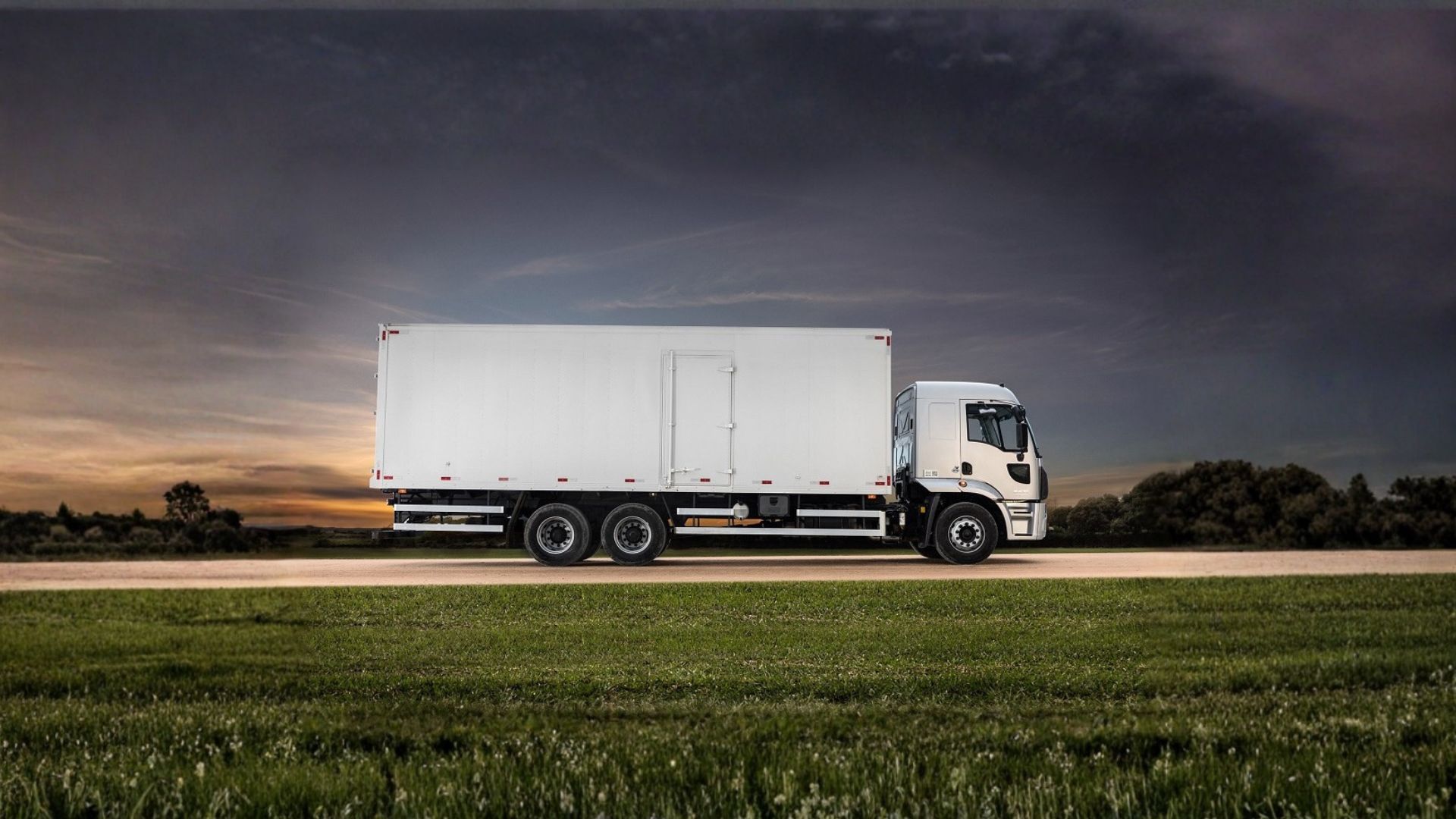 White box truck driving on a rural road at dusk under a dark sky