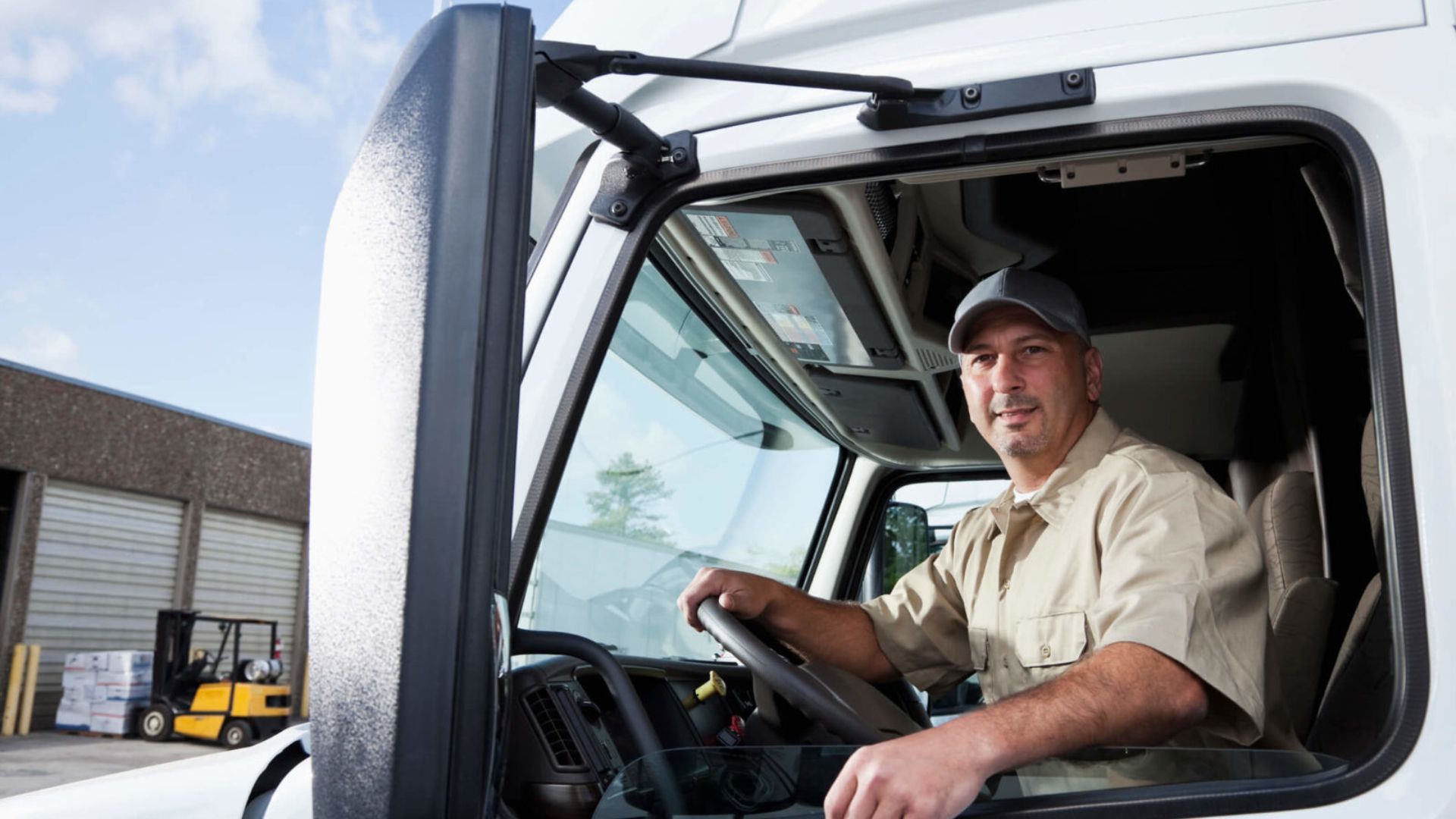Truck driver smiling in the cab of a white utility truck, with a warehouse in the background