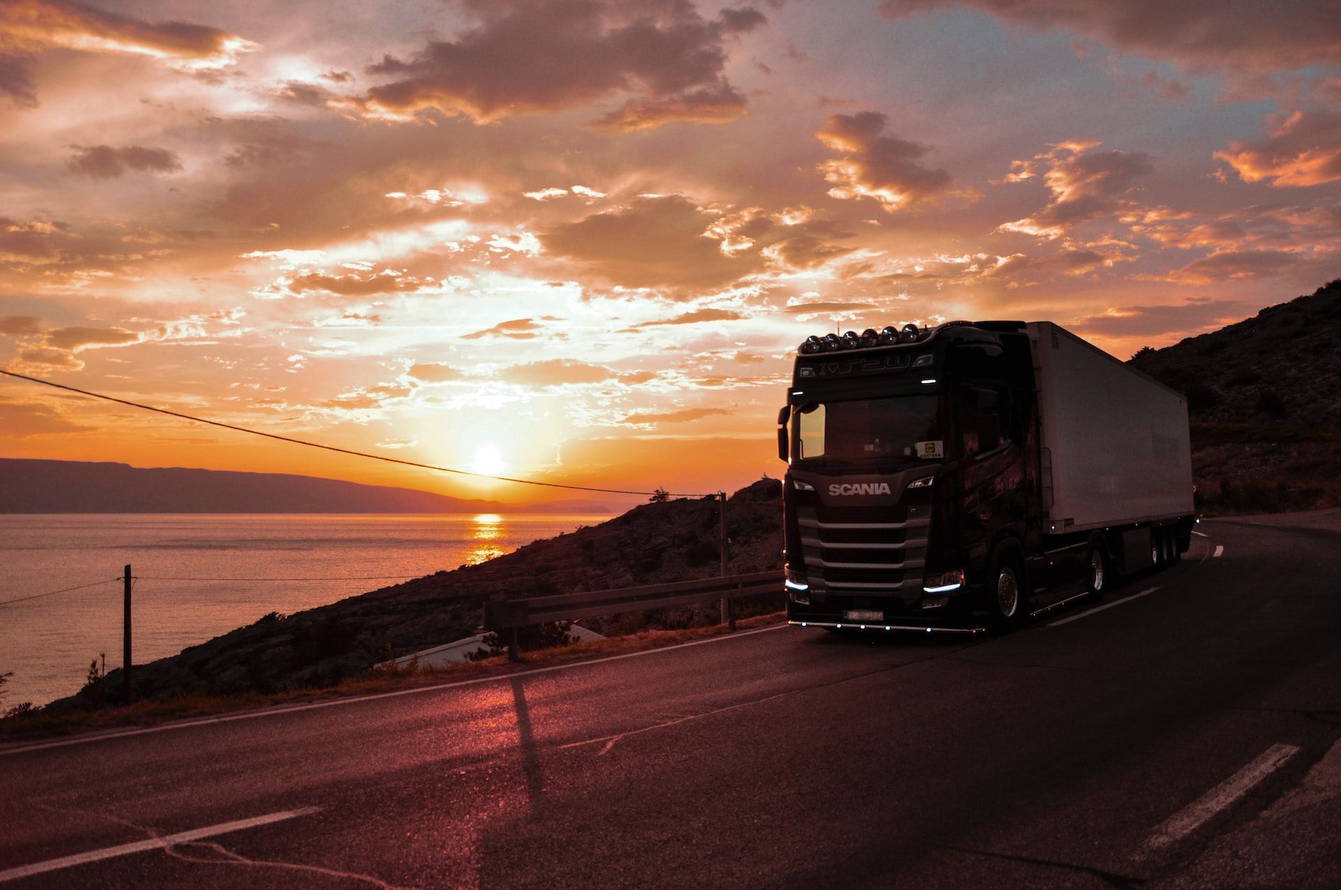 Truck on a coastal road at sunset with orange clouds and a glowing horizon