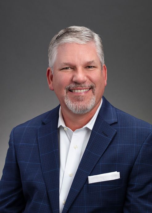 A man in a blue suit and white shirt is smiling for the camera.