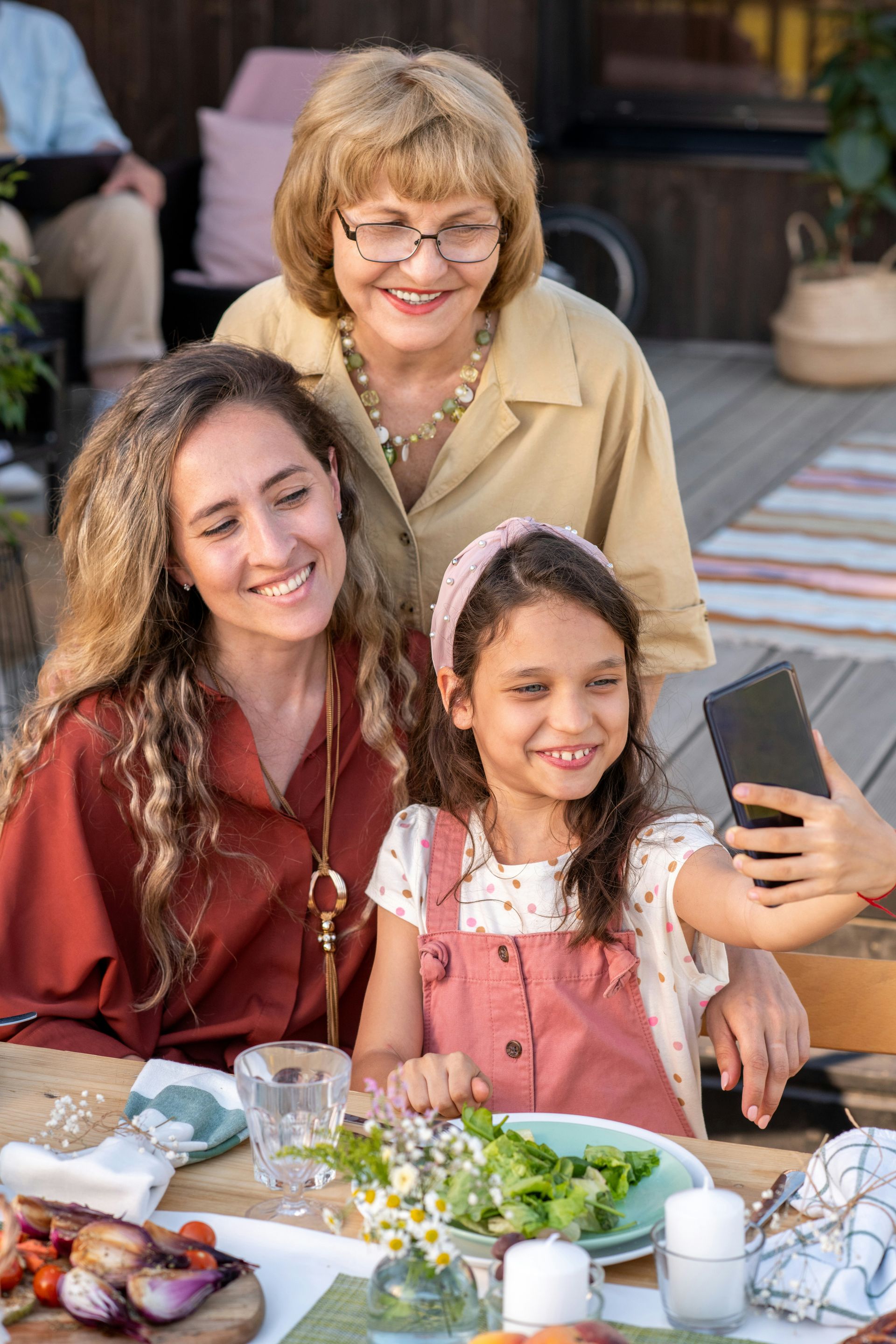 A family is sitting at a table taking a selfie with a cell phone.
