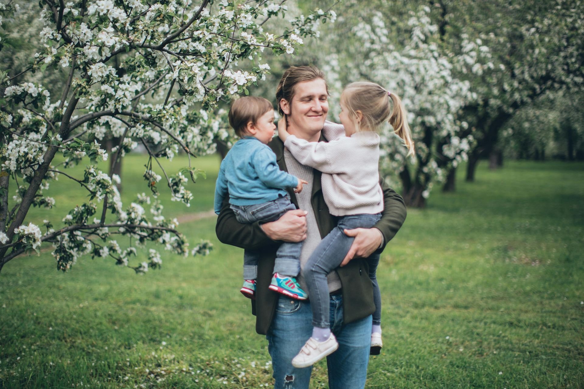 A man is holding two children in his arms in a park.
