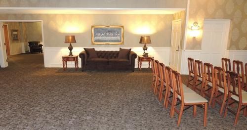 Carpeted lounge with a sofa, lamp, wall art, and rows of wooden chairs on the right
