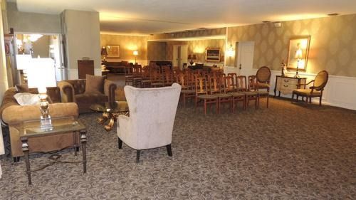 Spacious lobby with patterned carpet, beige chairs, side tables, and warm lighting under chandeliers
