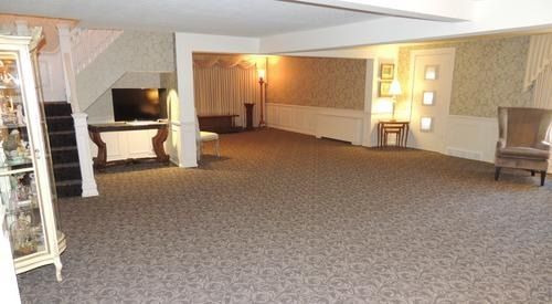 Spacious carpeted lobby with seating, staircase, and lamps in warm lighting