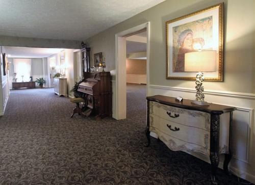Hotel hallway with patterned carpet, mirrored dresser, framed art, and open rooms leading to a bright lounge