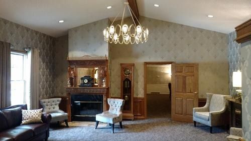 Elegant living room with fireplace, chandelier, patterned wallpaper, and seating by a large window