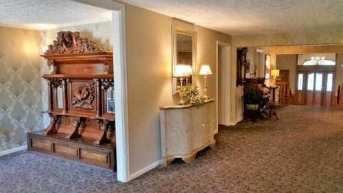 Long carpeted hallway with a wooden fireplace on the left and a side table with lamp on the right