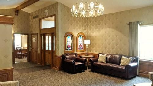 Elegant living room with brown leather sectional, chandelier, patterned wallpaper, and stained glass windows