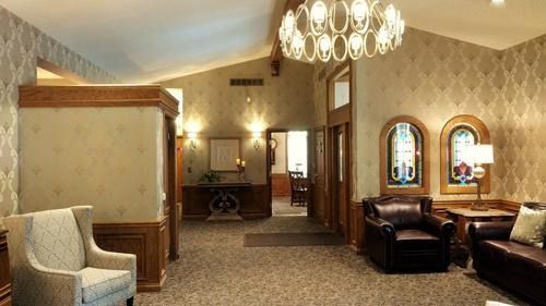 Elegant waiting room with patterned wallpaper, chandelier, leather chairs, and a reception desk.