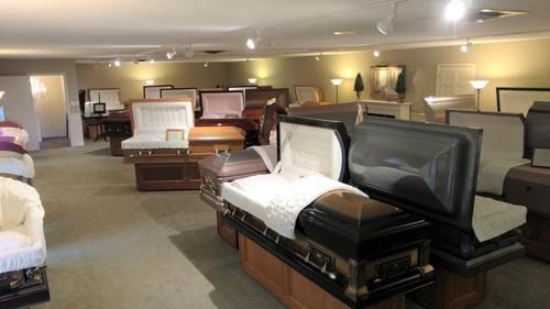 Showroom of coffins and caskets displayed under warm lighting in a funeral home showroom