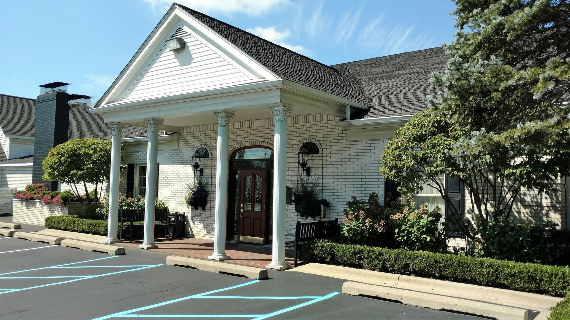 White storefront with columns and peaked roof beside parking spaces on a sunny day