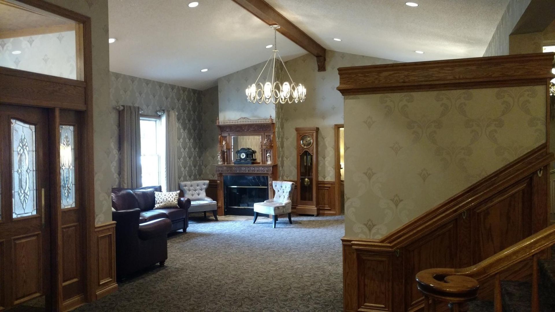 Spacious lobby with carpet, leather chairs, chandelier, wood beams, and staircase railing