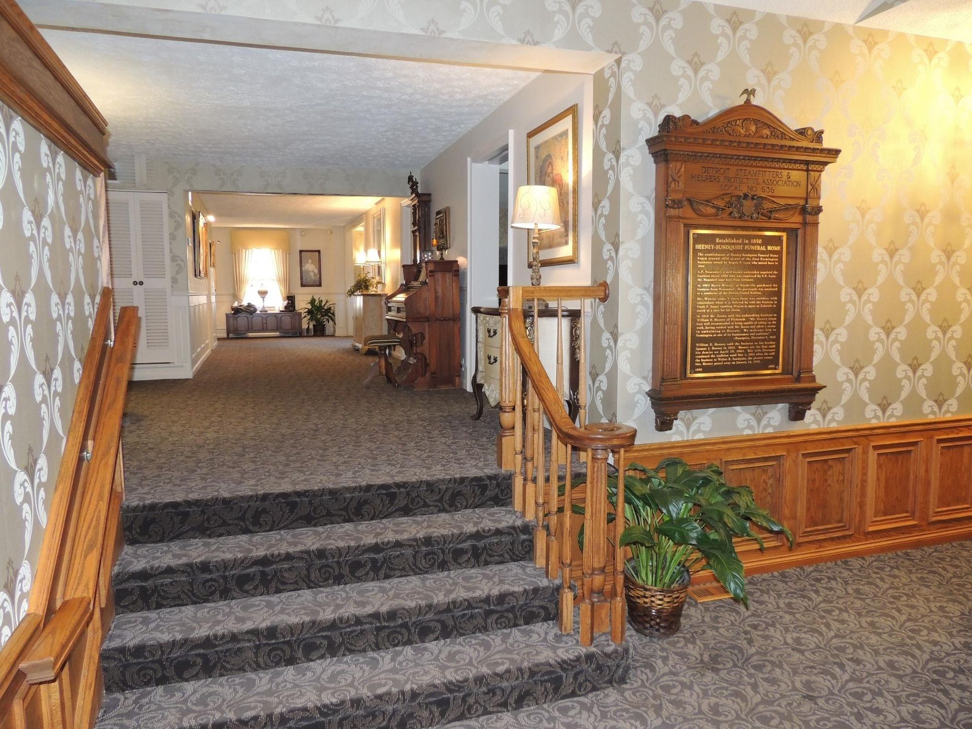 Carpeted hotel hallway with stairs, wood paneling, and a decorative wall cabinet.