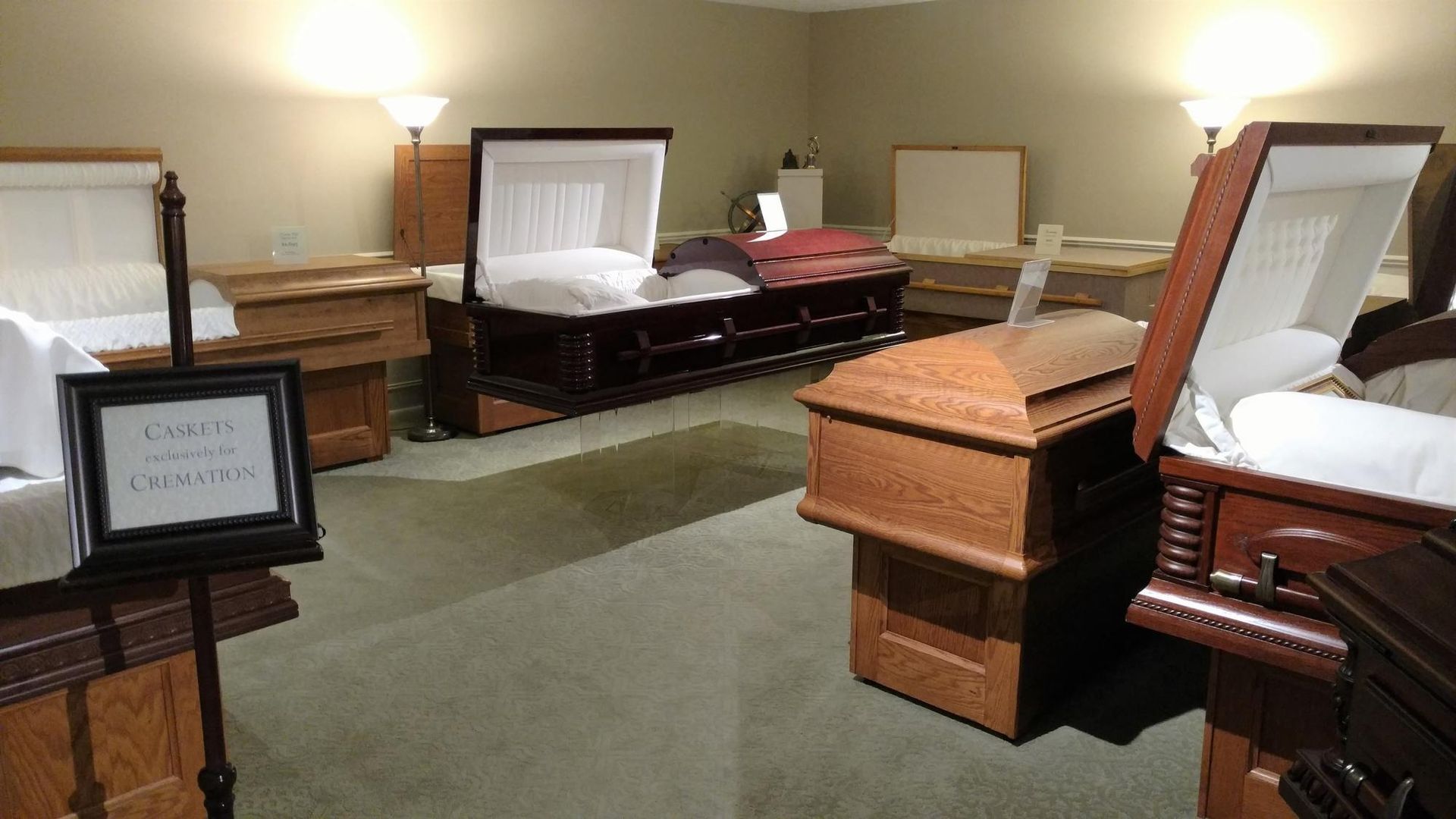 Open casket funeral room with white-lined coffins and wood furniture under warm lighting