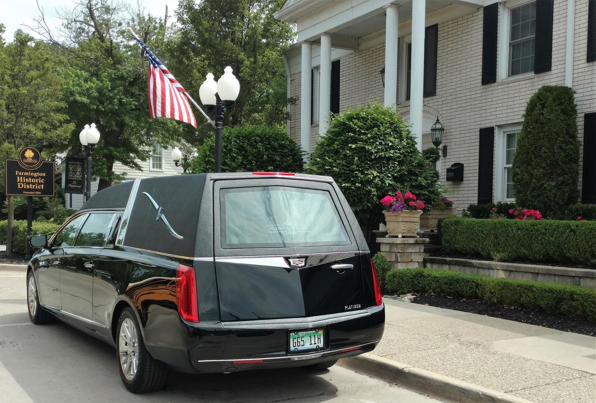 Black hearse parked outside a white-columned building with an American flag and landscaped entrance