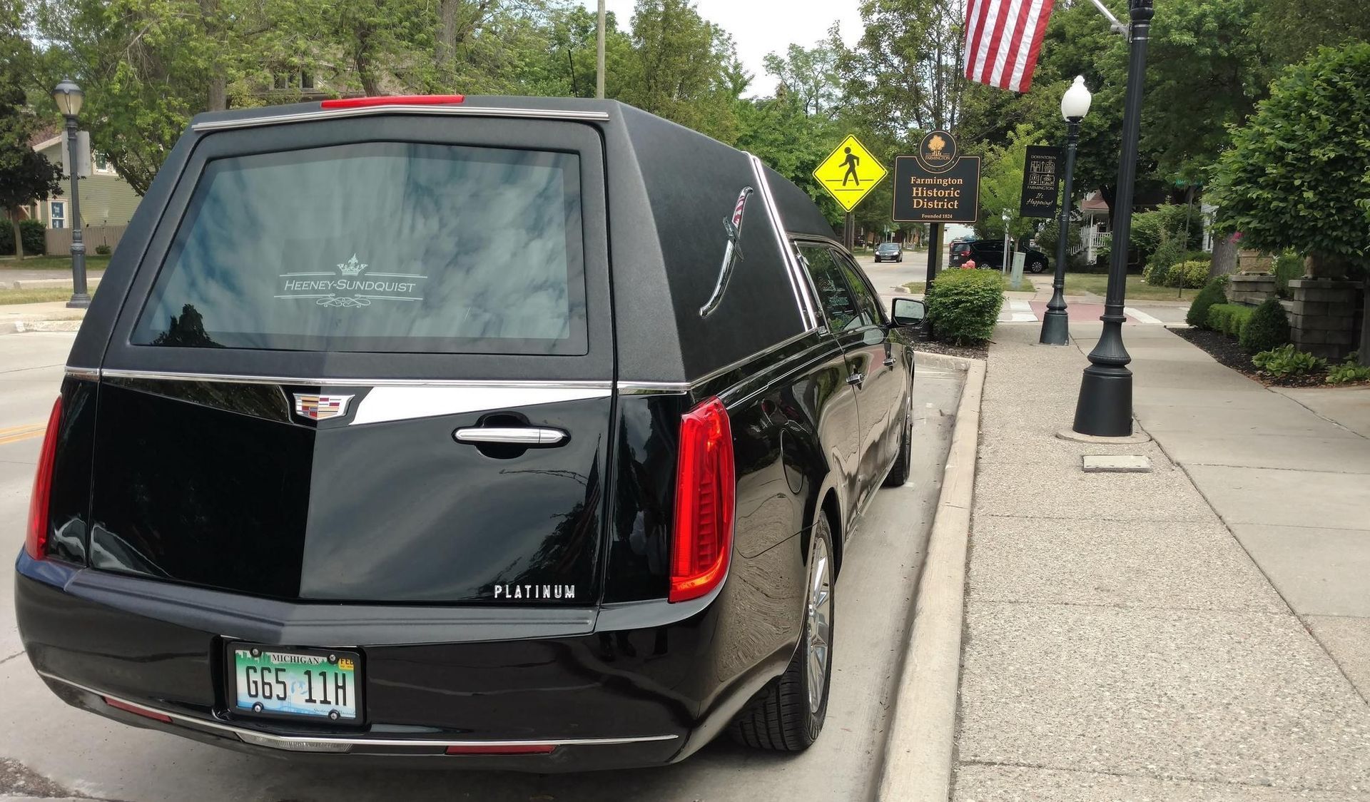 Black hearse parked on a city street beside a sidewalk and trees.