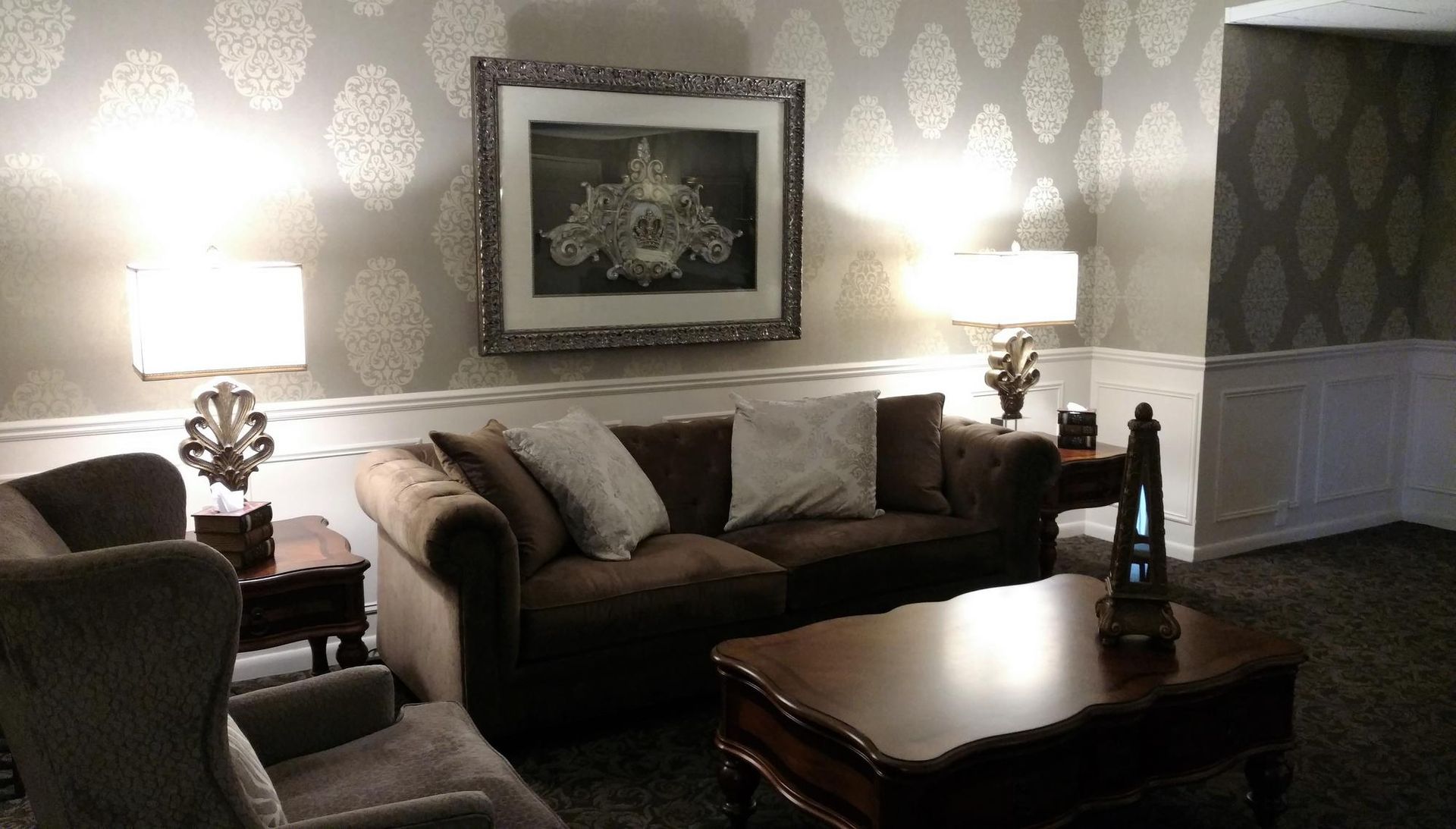 Elegant living room with patterned wallpaper, sofa, lamps, and a coffee table beneath framed wall art