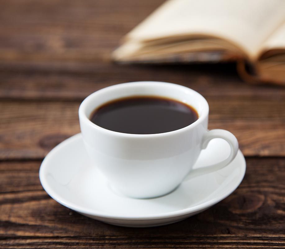 White coffee cup on saucer beside an open book on a wooden table