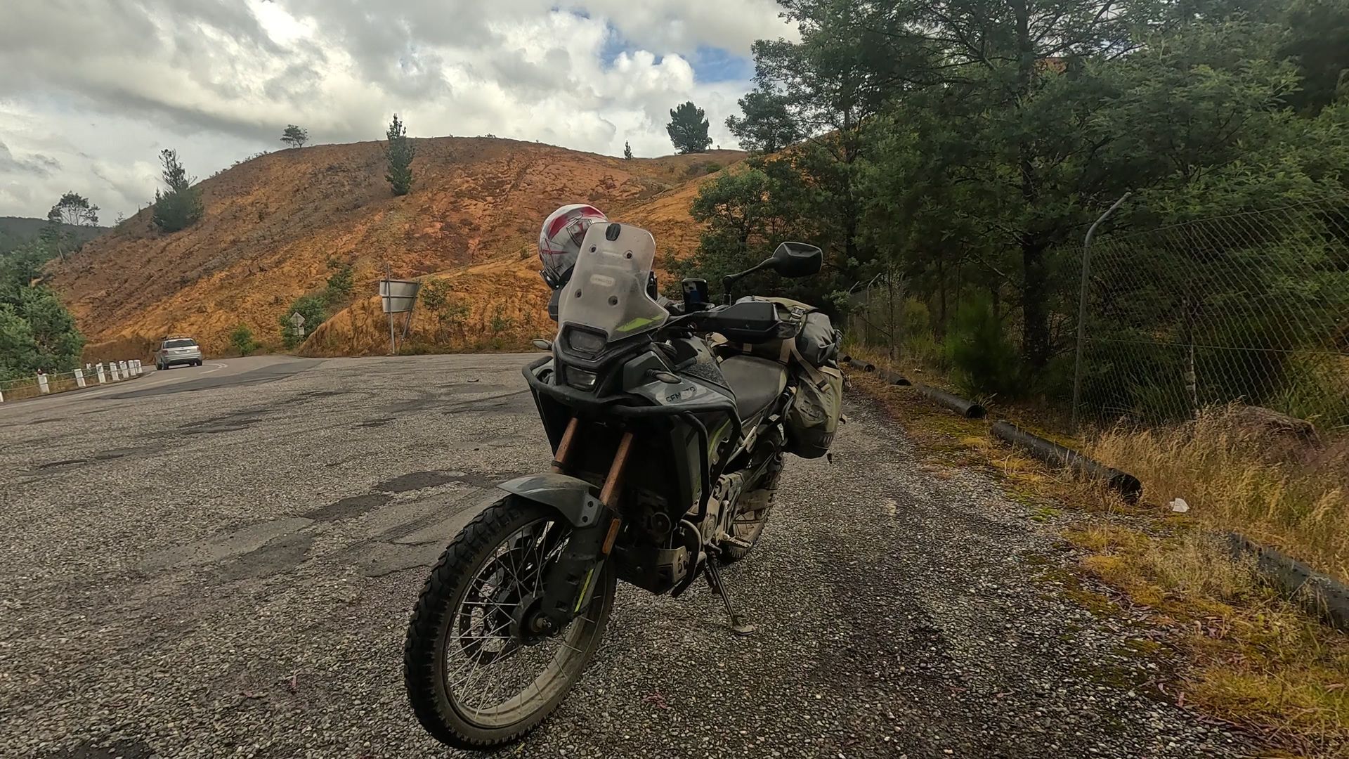 A motorcycle parked on gravel near a muddy hillside under cloudy skies.